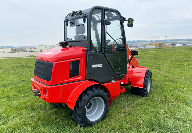 Toyo 850AT Teleskoplader mit Kabine Roter Toyo850AT Teleskoplader mit geschlossener Kabine auf einer grünen Wiese, Seitenansicht des kompakten Laders für Bau und Landwirtschaft.